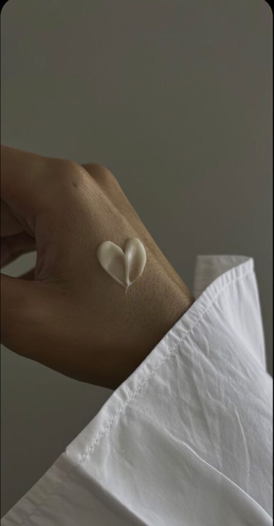 Heart-shaped cream on hand, symbolizing skincare love and care. White shirt in the background.