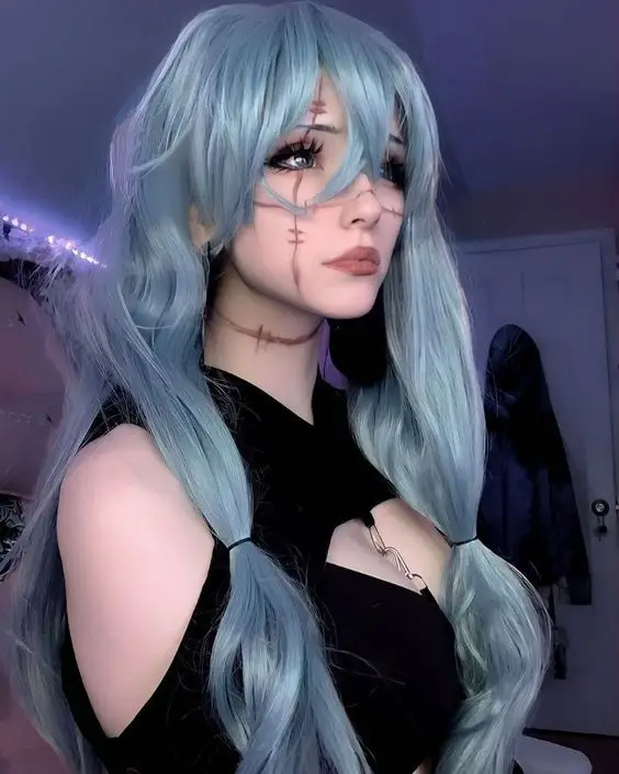 Cosplayer with long blue hair and stitch-like face makeup in a dimly lit room, wearing a black outfit.