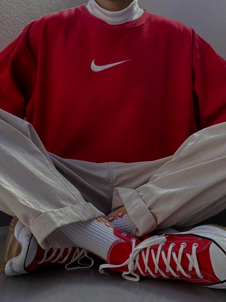 Casual style: person wearing red Nike sweatshirt, beige pants, and red sneakers, sitting cross-legged. Fashion streetwear vibe.