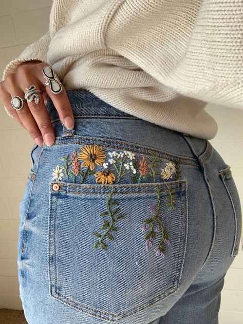 Stylish denim jeans with colorful floral embroidery on the back pocket. Casual fashion with unique accessory rings. Trendy and chic.