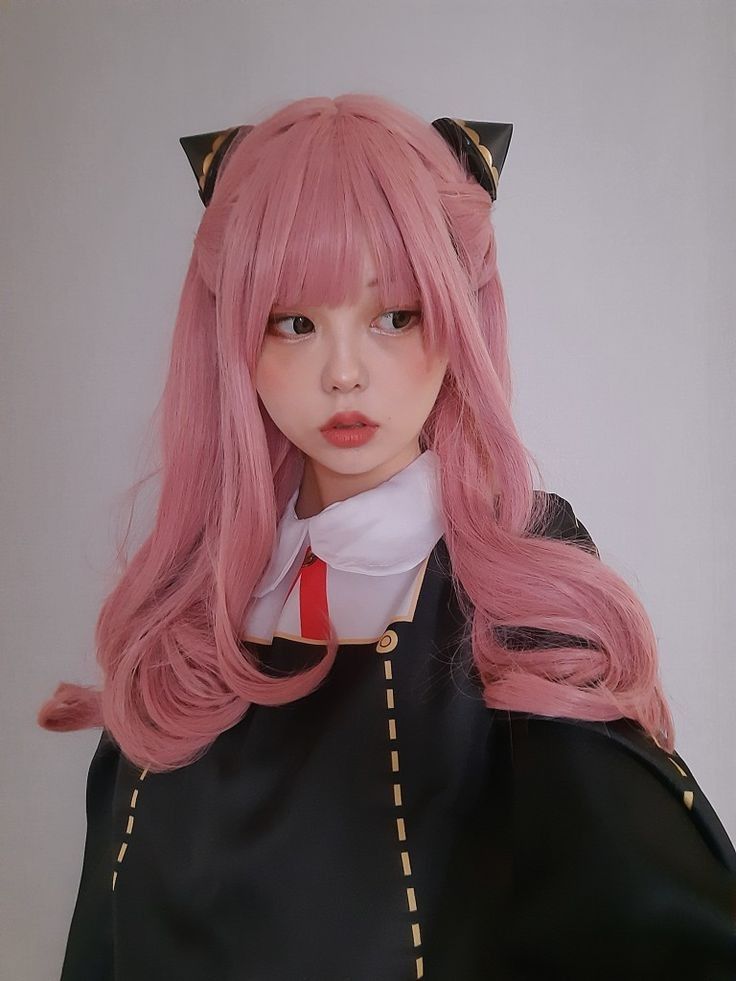 Cosplayer with pink hair and cat ear headband in anime-inspired outfit, looking to the side.