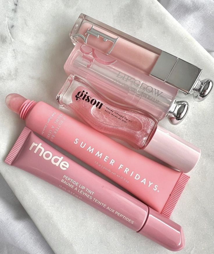 Assorted pink lip care products on marble surface; includes glosses and balms for moisturized, glossy lips.