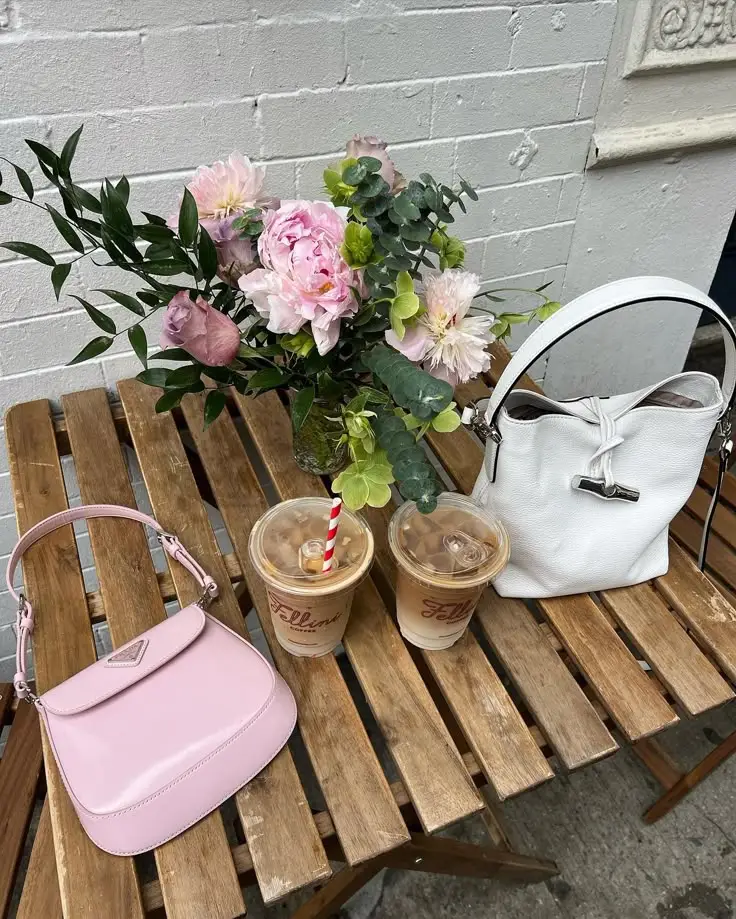 Chic outdoor café setting with iced coffees, pink and white handbags, and fresh flowers on a wooden table.