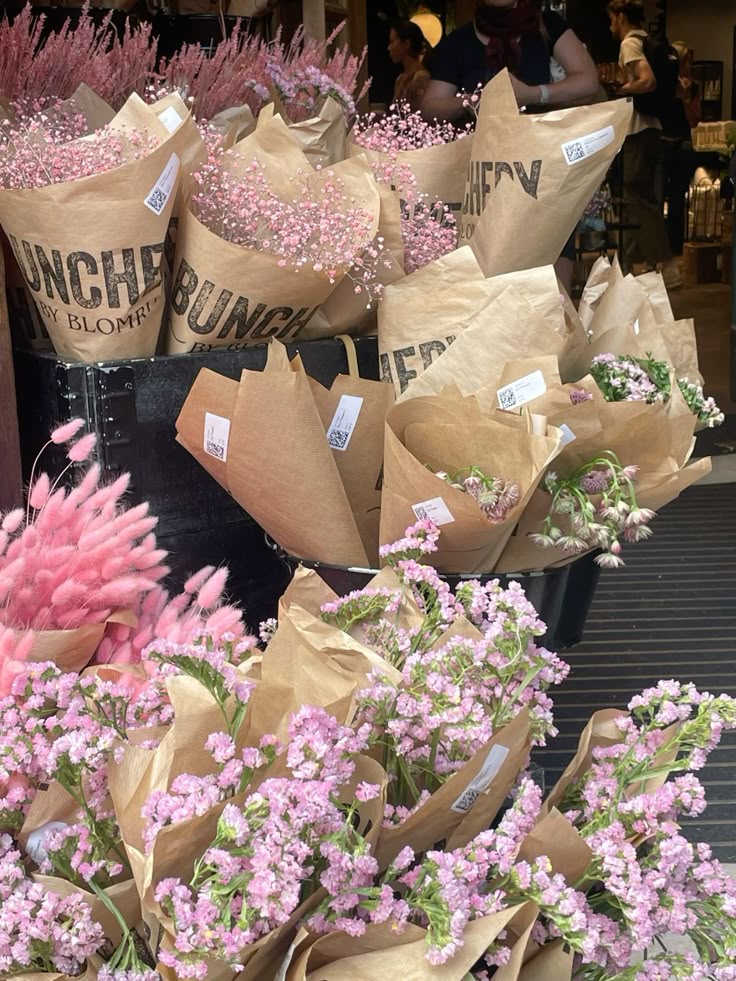 Bouquets of pink flowers wrapped in brown paper on display at a flower shop, creating a vibrant and inviting market scene.