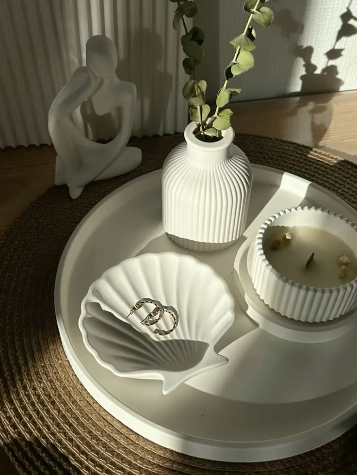 Modern decor with a white figurine, ribbed vase, candle, and shell dish on a round tray. Elegant, warm-toned interior styling.