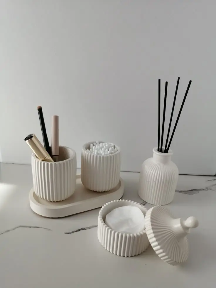 Elegant bathroom set with ribbed ceramic organizers, holding makeup, cotton swabs, and diffuser on a marble countertop.