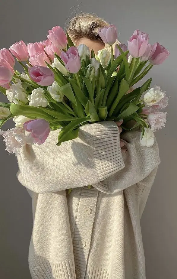 Person in cozy sweater holding a vibrant bouquet of pink and white tulips, creating a warm and inviting springtime vibe.