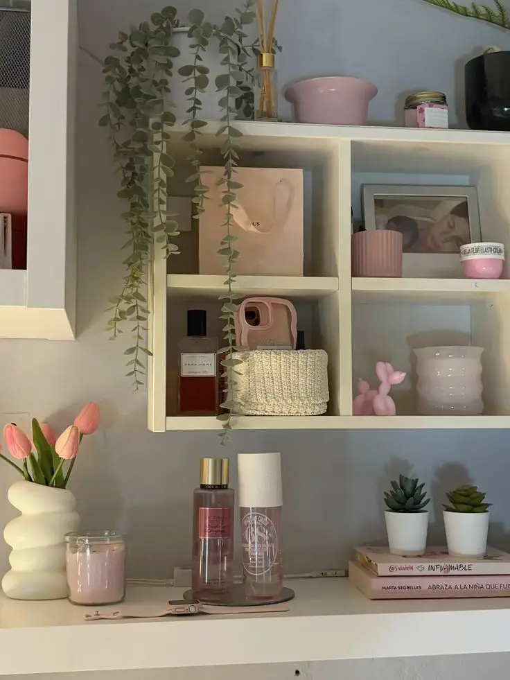 Chic shelf with pink decor, plants, perfume, and books, adding elegance to a cozy room environment.