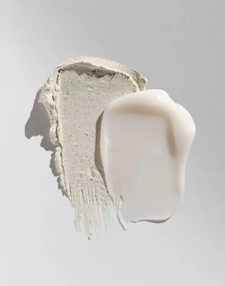 Texture comparison of a beige clay mask and a creamy white moisturizer on a white background.