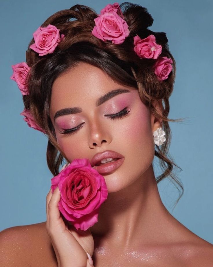 Woman with pink makeup and roses, holding a rose, on a blue background. Romantic floral beauty concept.