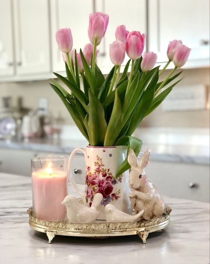 Pink tulips in floral jug, candle, bird and rabbit figurines on tray, kitchen setting. Elegant spring decor.