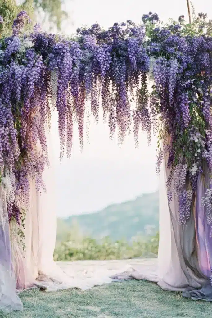 Lavender floral arch with cascading flowers set against a serene countryside backdrop, perfect for weddings or outdoor events.