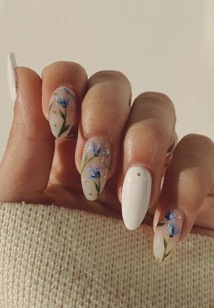 Elegant floral nail art with blue flowers and gold accents, featuring long almond-shaped nails on a neutral background.