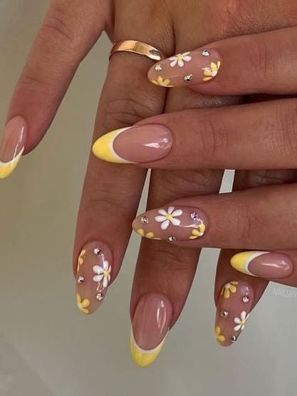 Elegant nails with yellow tips and white flower designs, accented with rhinestones, showcasing chic, modern nail art.