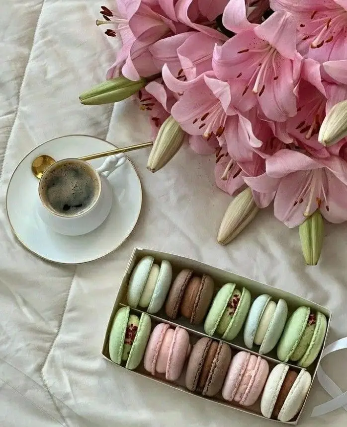 Elegant setup with pink lilies, assorted pastel macarons, and a cup of coffee on a white background. Perfect for a cozy morning.