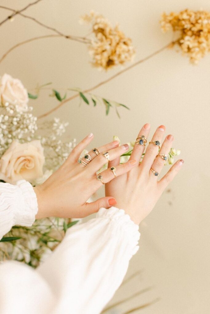 Elegant hands adorned with gold rings against a floral background, showcasing delicate jewelry design.