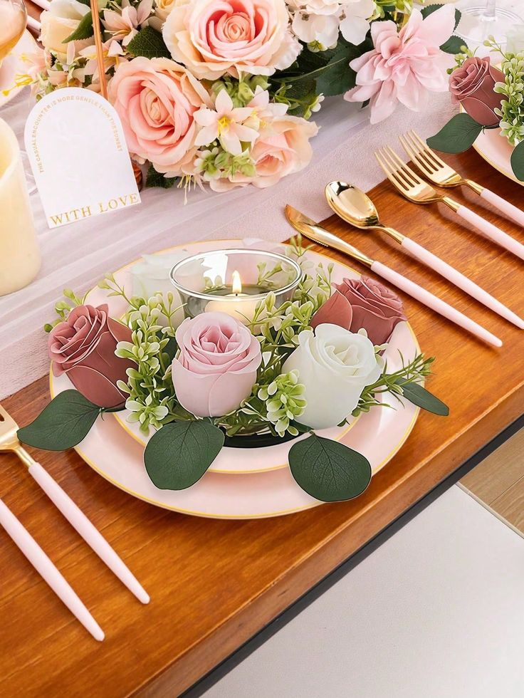 Elegant table setting with pink roses, greenery, and a candle centerpiece on a wooden table, perfect for weddings or romantic dinners.