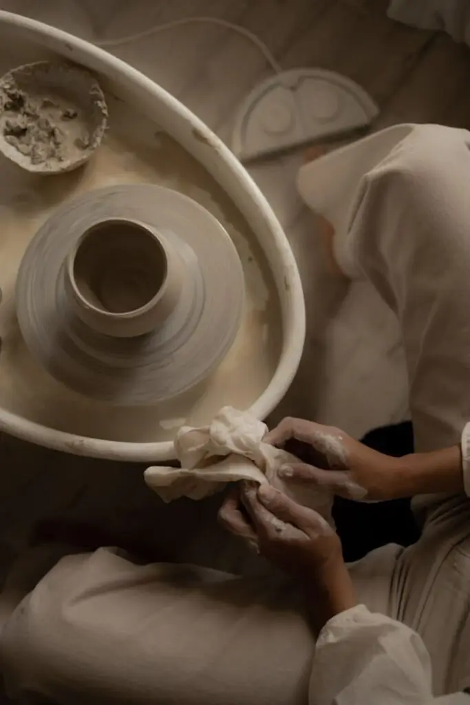 Person crafting pottery on a spinning wheel, close-up of hands shaping clay, showcasing pottery-making process.