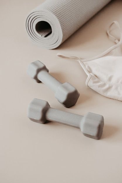 Gray dumbbells, rolled yoga mat, and workout clothes on beige background. Perfect fitness setup for home workouts and yoga sessions.