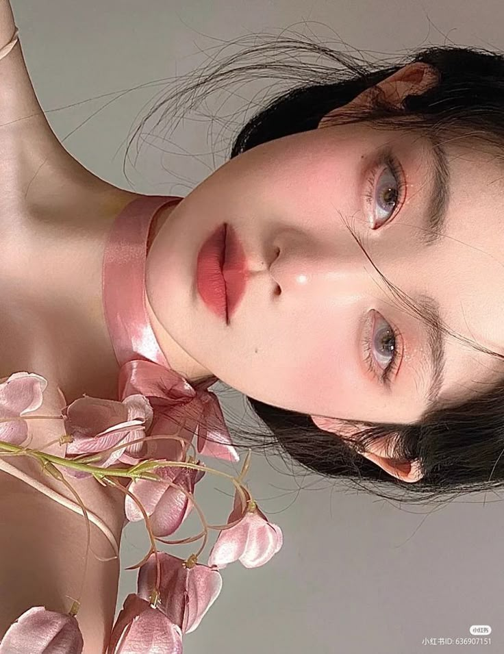 Woman with soft makeup holding pink flowers, delicate and serene look.