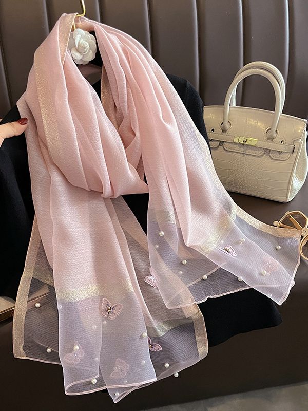 Elegant pink scarf with butterfly details and pearls, styled with a beige handbag on a black background. Perfect for fashion lovers.