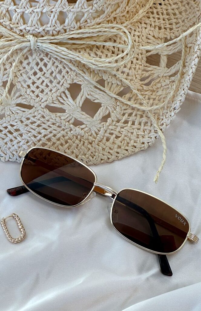 Stylish sunglasses on white fabric, with a woven accessory and a small sparkling earring. Perfect for summer fashion vibes.