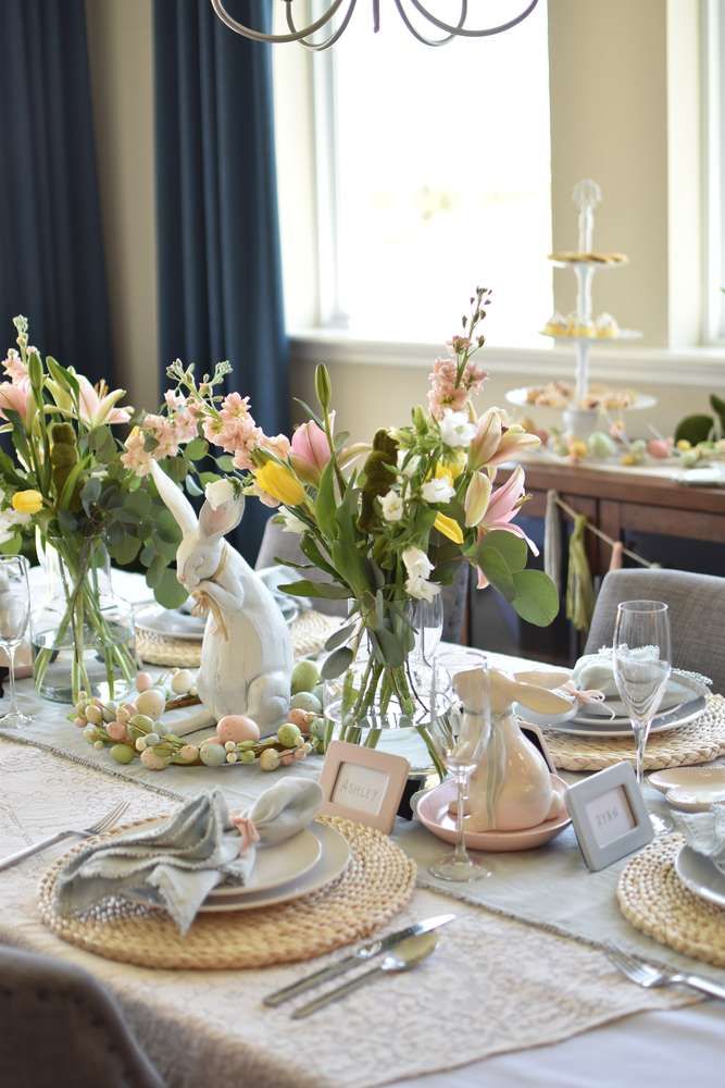 Elegant Easter table setting with floral centerpieces, decorative bunny figurines, pastel eggs, and woven placemats.