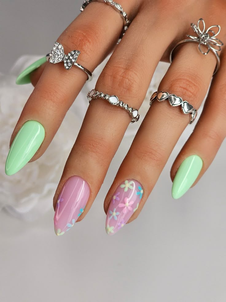 Pastel green and pink floral nail art with silver rings on fingers, showcasing stylish summer manicure.