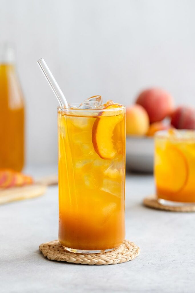 Refreshing iced peach tea served in a glass with a straw, garnished with peach slices, perfect for a summer drink.