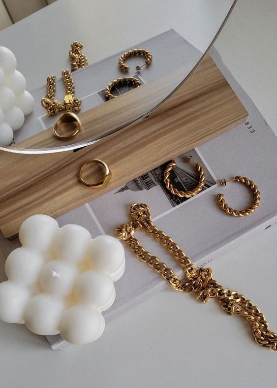 Gold jewelry and modern white candle on a book with wooden accents, reflecting minimalistic elegance and style.