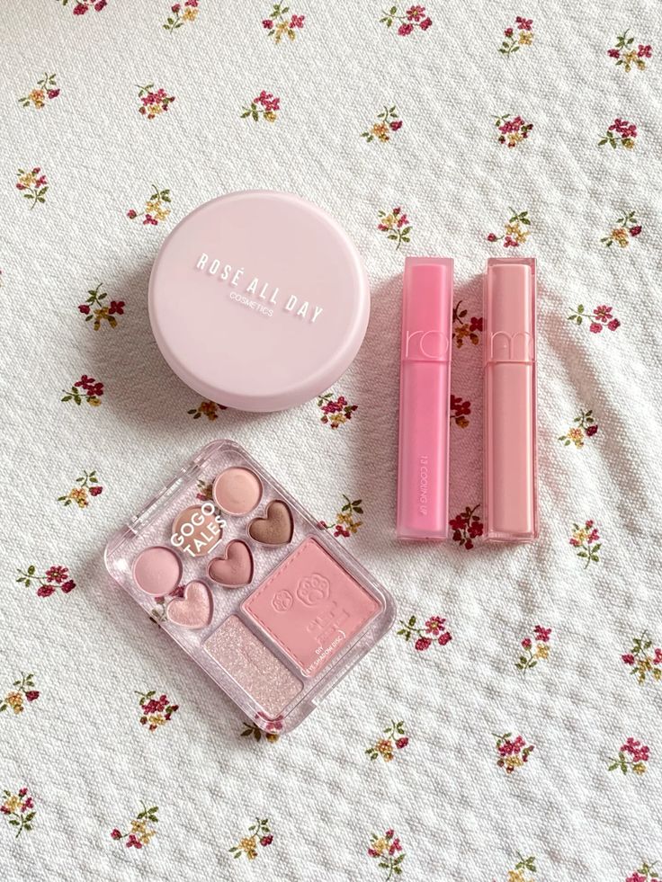 Pink cosmetics set on floral fabric: blush, lipsticks, and eyeshadow palette, ideal for a soft, romantic makeup look.