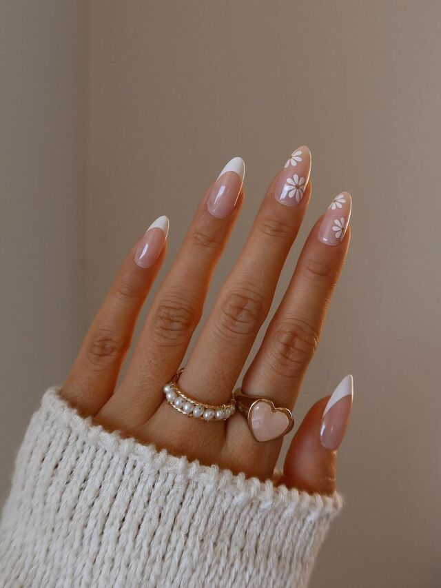 Elegant French manicure with floral designs and gold rings, hand in cozy white sweater. Perfect fashion and nail art inspiration.