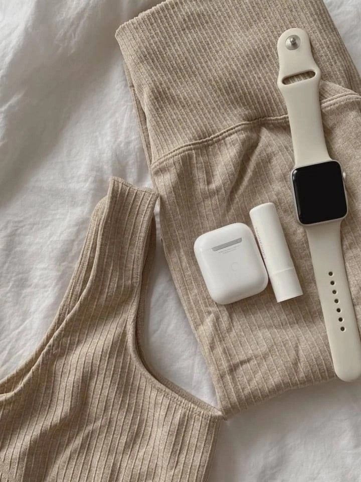 Beige ribbed activewear with smartwatch, earbuds, and lip balm on white sheet, stylish workout essentials.