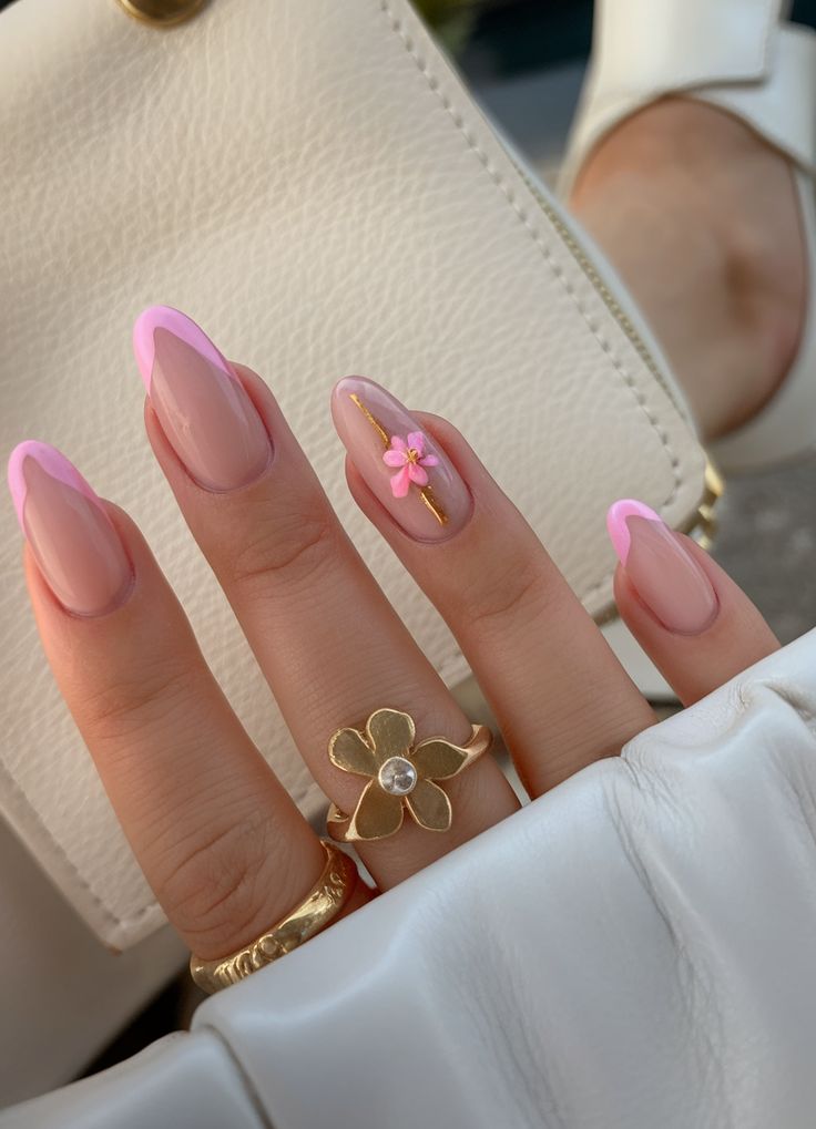 Elegant hand with pink french manicure, floral accent, and gold rings, holding a white purse. Classy nail art and accessories.