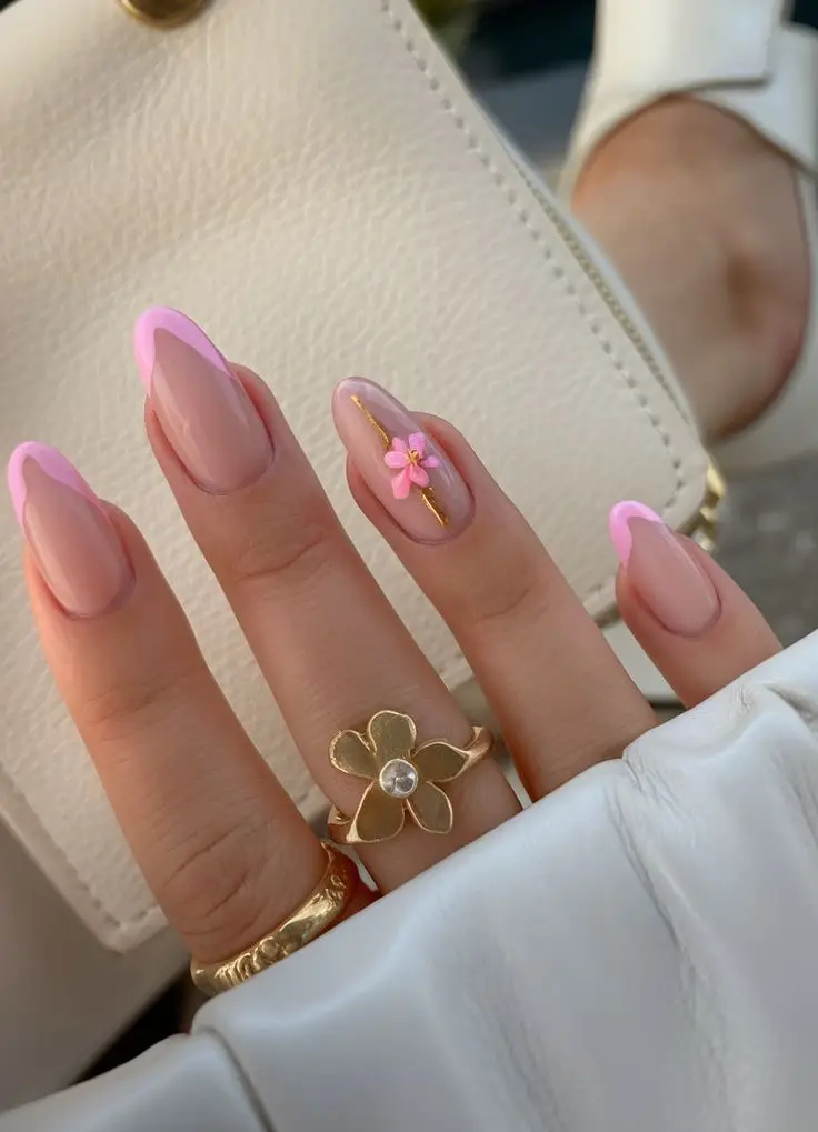 Elegant hand with pink french manicure, floral accent, and gold rings, holding a white purse. Classy nail art and accessories.