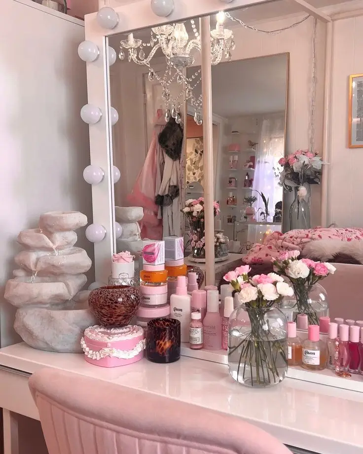 Vanity table with skincare products, pink decor, and fresh flowers, reflecting cozy elegance and style in a chic bedroom setting.
