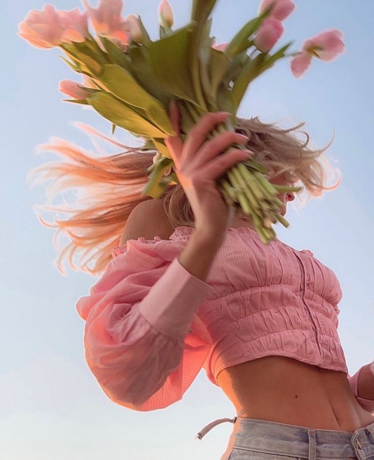 Woman in pink top holding tulips under a clear blue sky, capturing a fresh spring vibe.