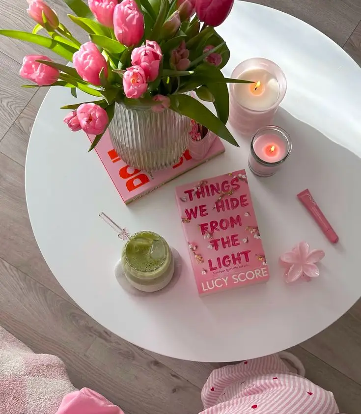 Cozy coffee table setup with pink tulips, candles, matcha drink, and a book titled Things We Hide From the Light by Lucy Score.