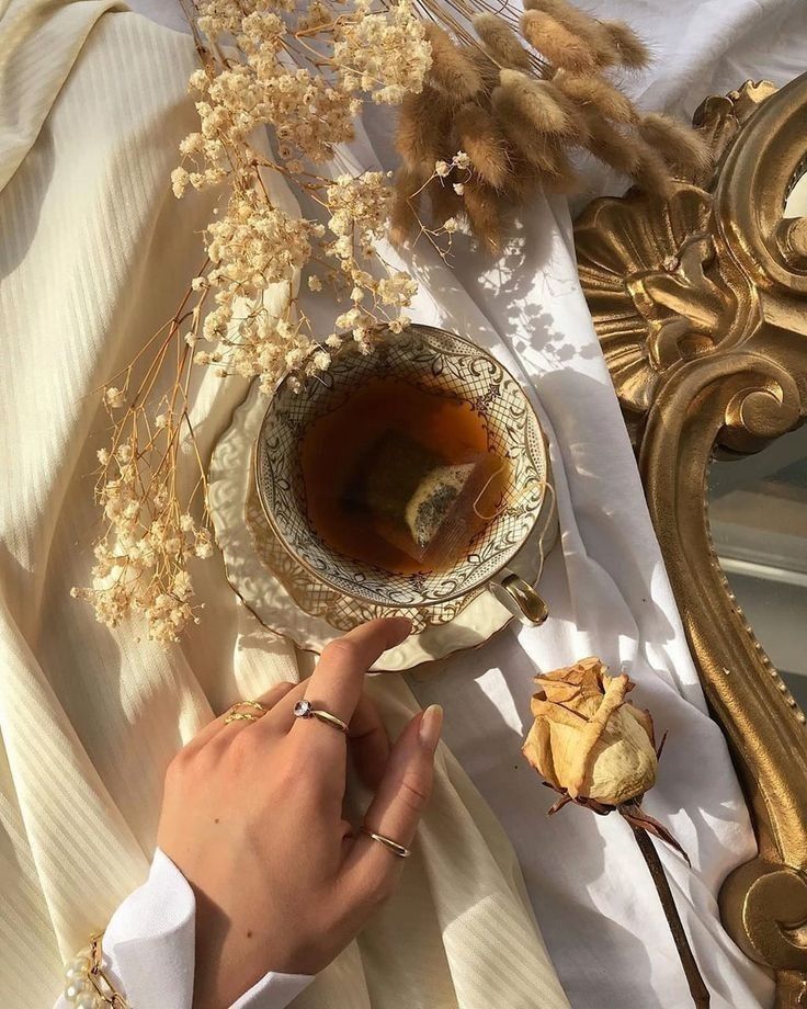 Elegant tea setting with a vintage cup, delicate dried flowers, and a woman's hand. Warm, cozy, and inviting ambiance.