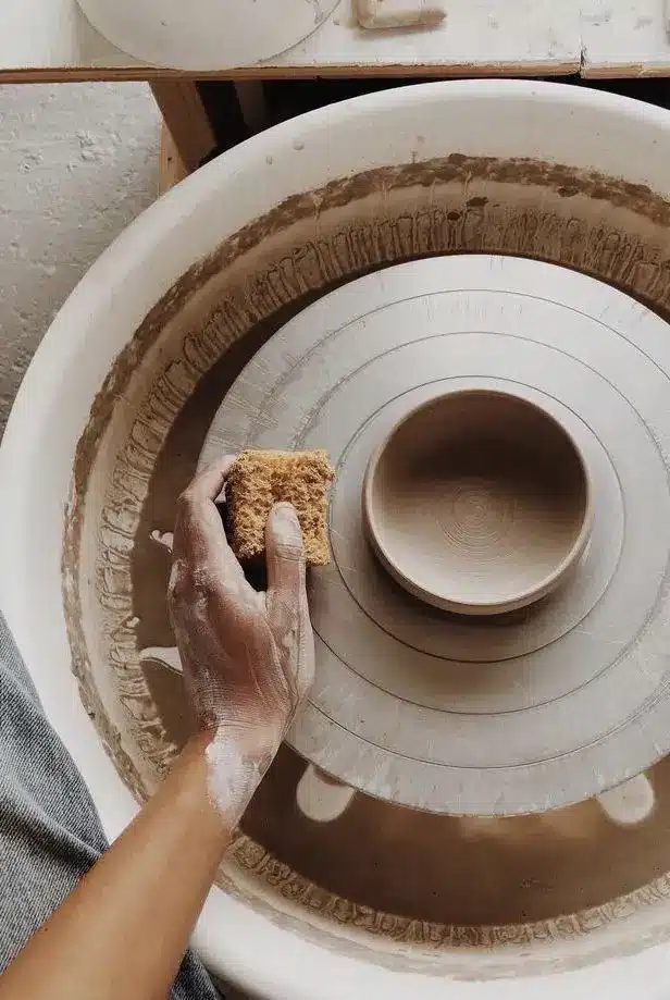 Hand crafting pottery on a wheel, sponge and clay in artist's studio. Creative ceramics process in action.