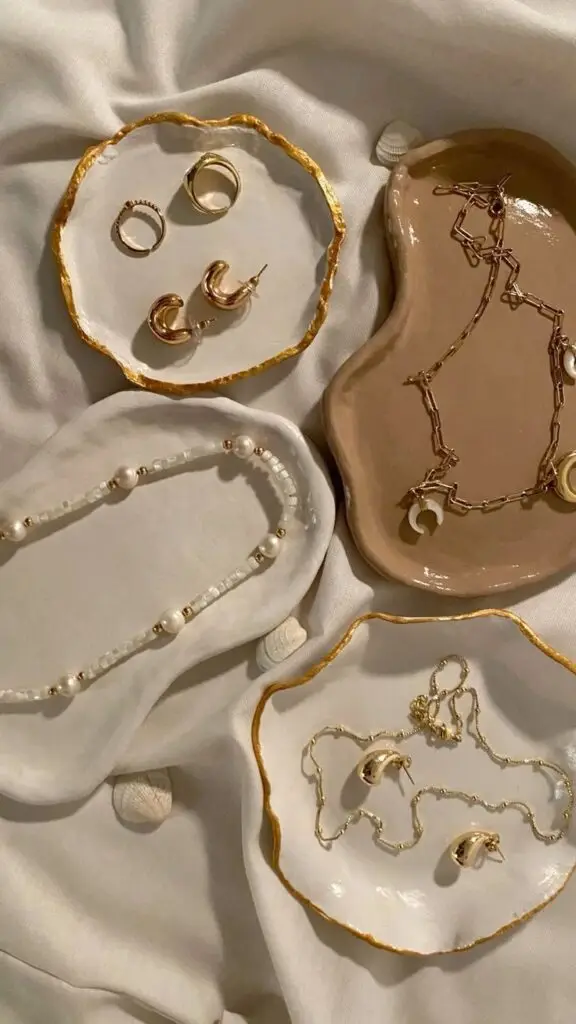 Elegant jewelry on decorative ceramic dishes with a satin fabric backdrop, showcasing necklaces, rings, and earrings.