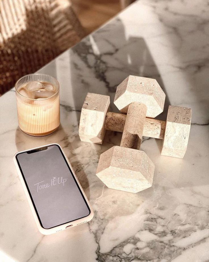 Marble table with stone dumbbells, iced coffee, and a smartphone displaying Tone It Up. Fitness and lifestyle concept.