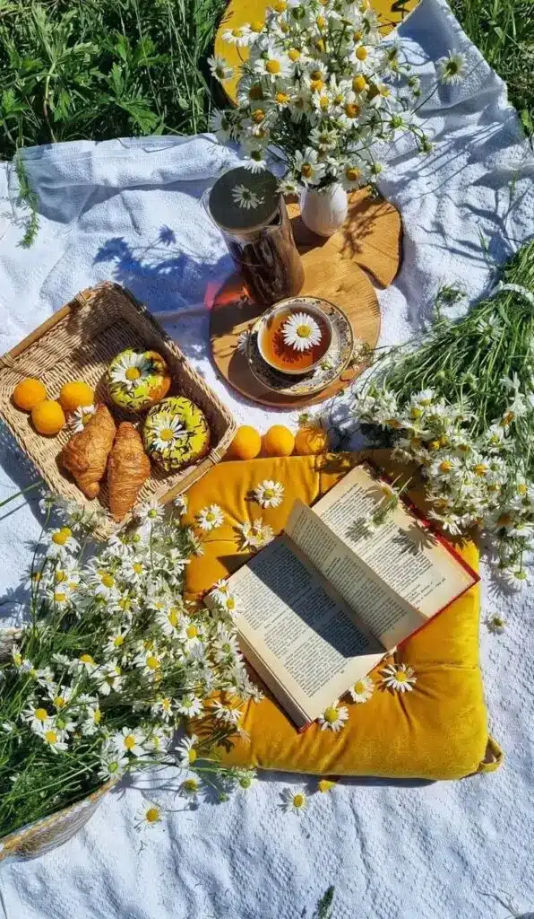 Sunny picnic scene with flowers, tea, croissants, and an open book on a blanket. Perfect for a summer day in nature.