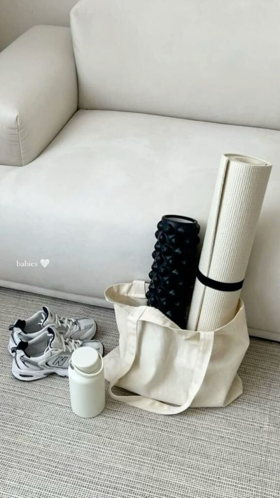 Yoga mat, foam roller, and sneakers by a couch on a carpet. Ideal fitness gear setup in a minimalist beige-themed room.