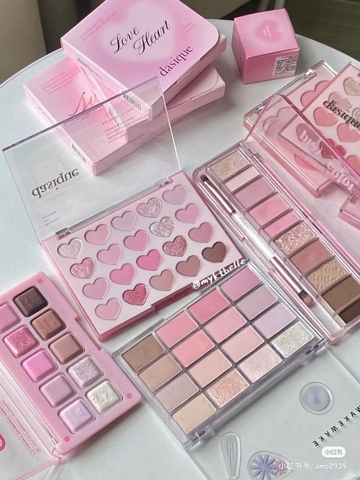 Various pink-themed eyeshadow palettes and boxes displayed on a white table.