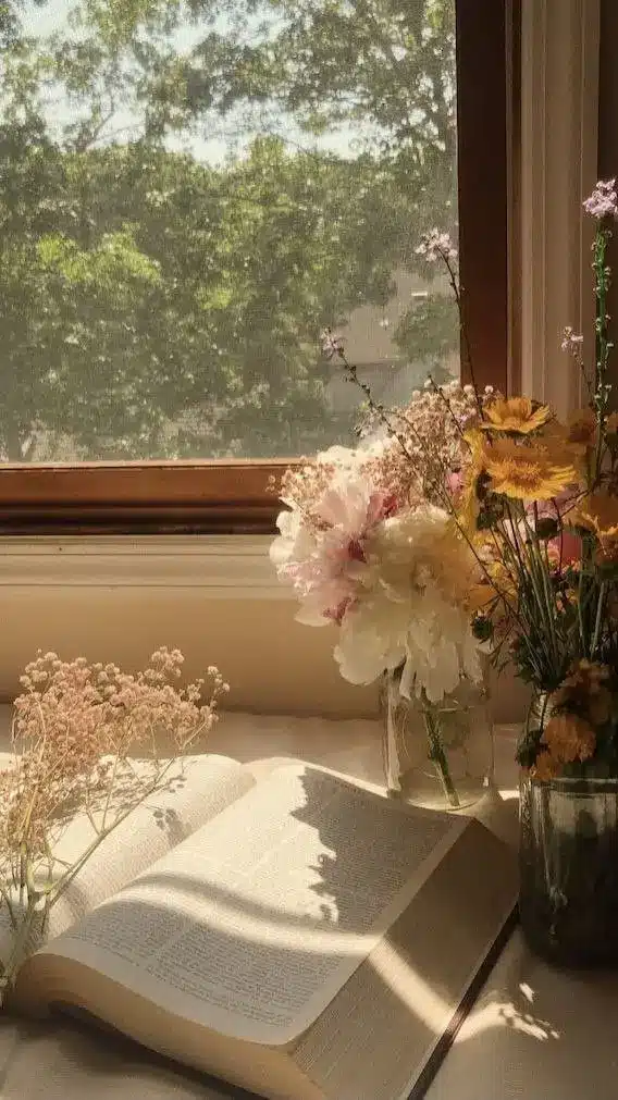 Open book with flowers and sunny window view, creating a cozy and peaceful reading nook ambiance.