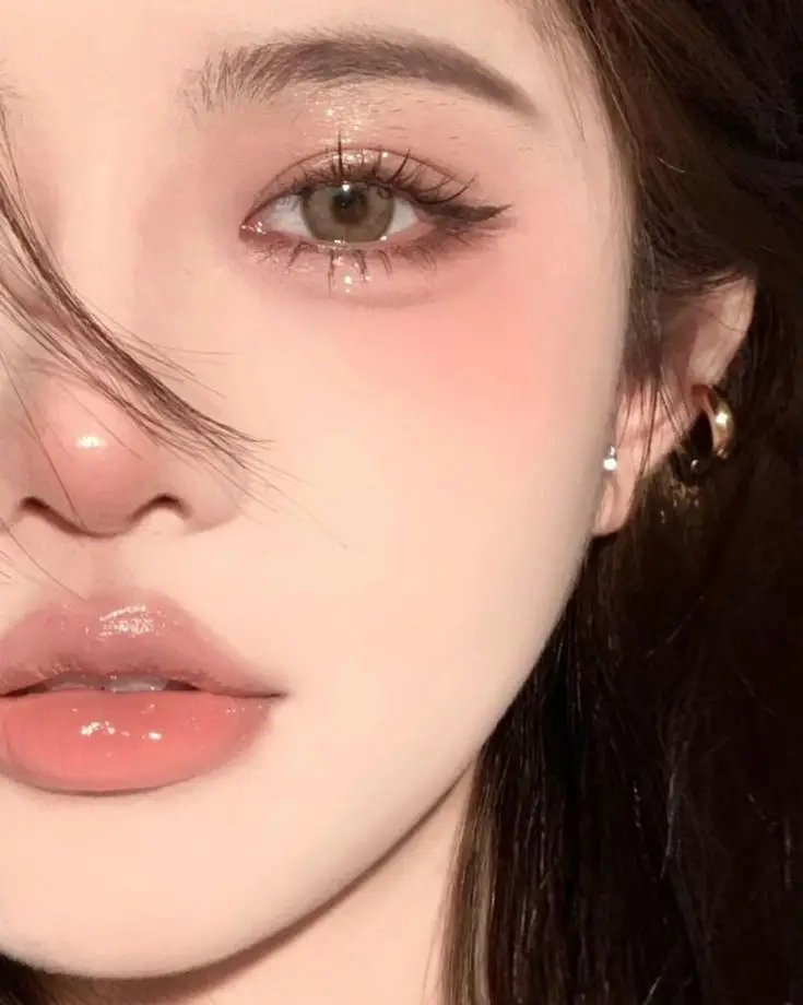 Close-up of a woman's eye and lips with glossy makeup, highlighting delicate features and a subtle beauty look.