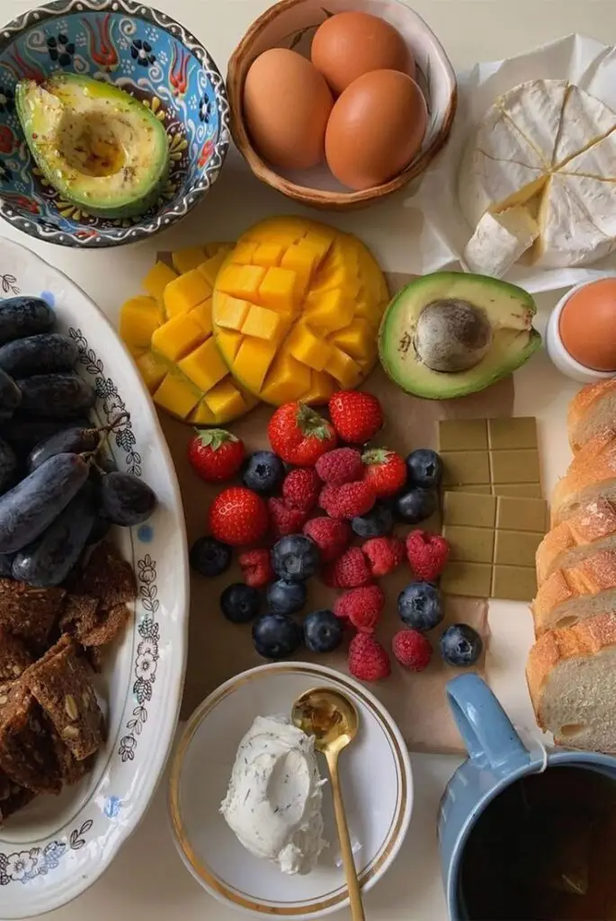 Assorted breakfast spread with fruits, bread, avocados, eggs, cheese, and tea. Perfect for a healthy and delicious start to the day.