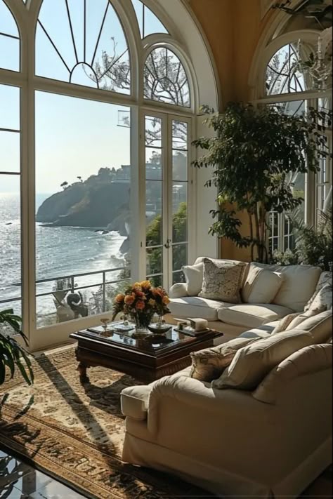 Luxurious living room overlooking the ocean with large arched windows, cozy couches, and vibrant plants, creating a serene coastal retreat.
