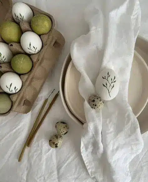 Decorative eggs with green designs, carton of green and white eggs, quail eggs, on white fabric with plates and sticks.